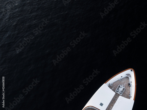 Photography High angle aerial bird's eye partial view of the bow of a long white luxury yacht with wooden deck in dark blue waters shortly after sunset in Sydney, Australia with a lot of copy space