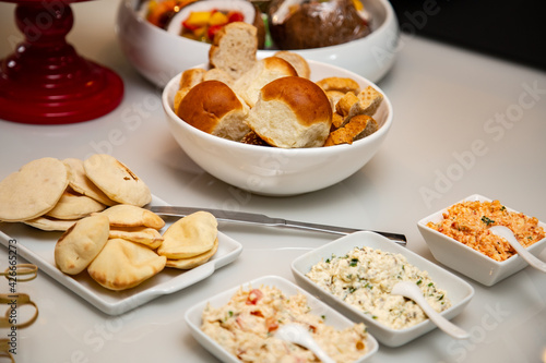 Uma vasilha com pães diversos e patês dispostos em uma mesa de buffet.