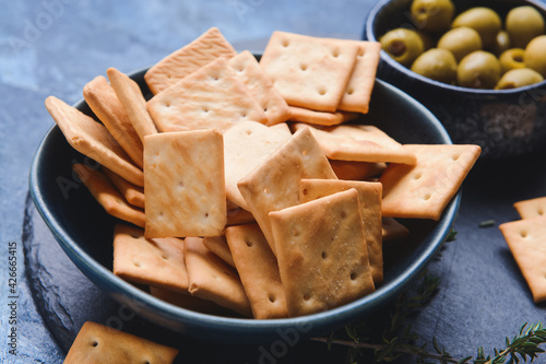 Bowl of crackers and olives on color background