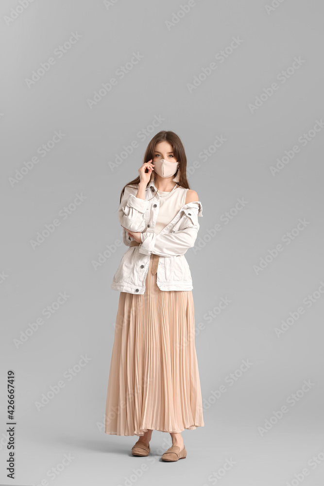 Fashionable young woman wearing mask on grey background Fashionable young woman wearing mask on grey background