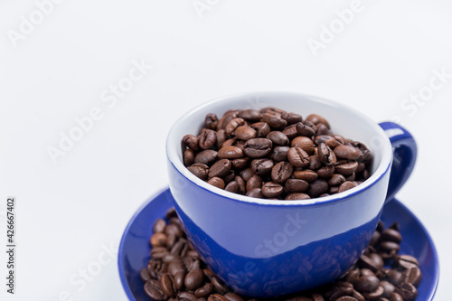 cup of coffee  close-up of a blue ceramic cup with white inside  on a plate with coffee beans on a white surface  horizontal photo