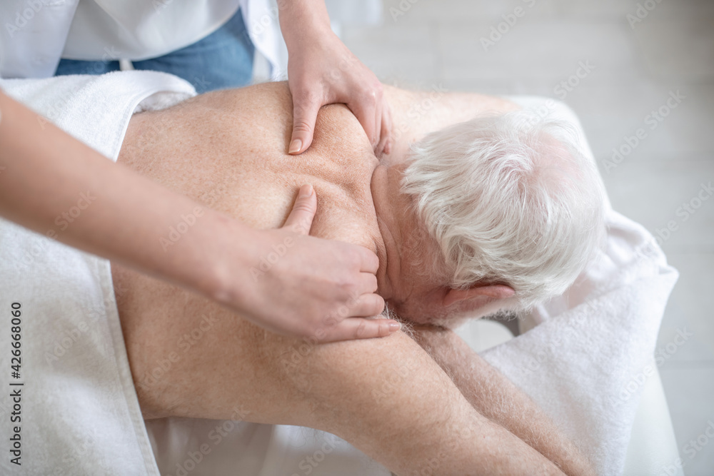 Massage therapist working with an elderly male patient Massage therapist working with an elderly male patient