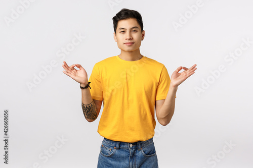 Find peace inside your sould. Calm and relieved, peaceful young handsome tattooed asian guy meditating, release stress, spread hands sideways with zen orbs, reach nirvana, feel patience photo