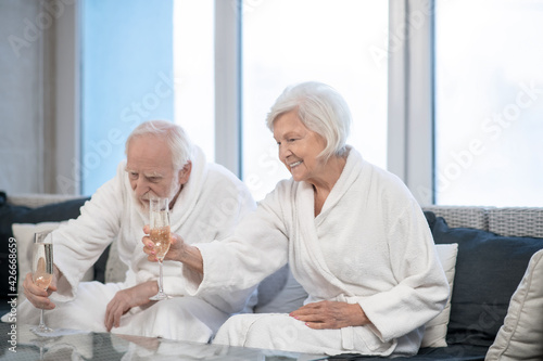 Bilde på lerret Senior couple in white robes drinking champagne and looking pleased