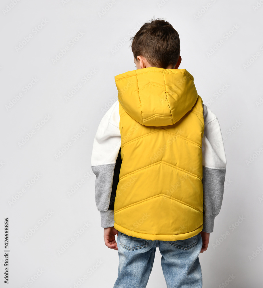 Back view of a teenage guy in a yellow vest, sleeveless down jacket with a hood and jeans. white background Back view of a teenage guy in a yellow vest, sleeveless down jacket with a hood and jeans. white background