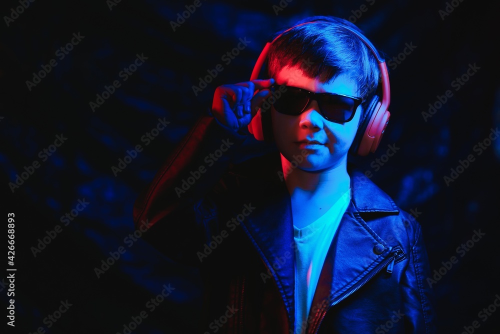 Studio shot in dark studio with neon light. Portrait of a stylish boy with headphones Studio shot in dark studio with neon light. Portrait of a stylish boy with headphones