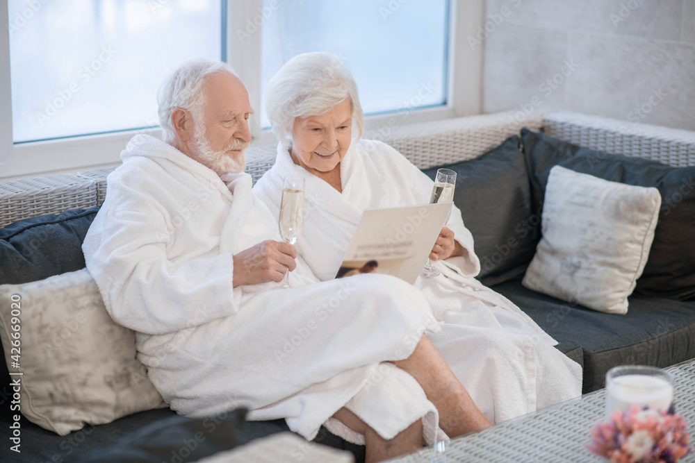 Senior couple in white robes having great times in spa salon and looking relaxed Senior couple in white robes having great times in spa salon and looking relaxed