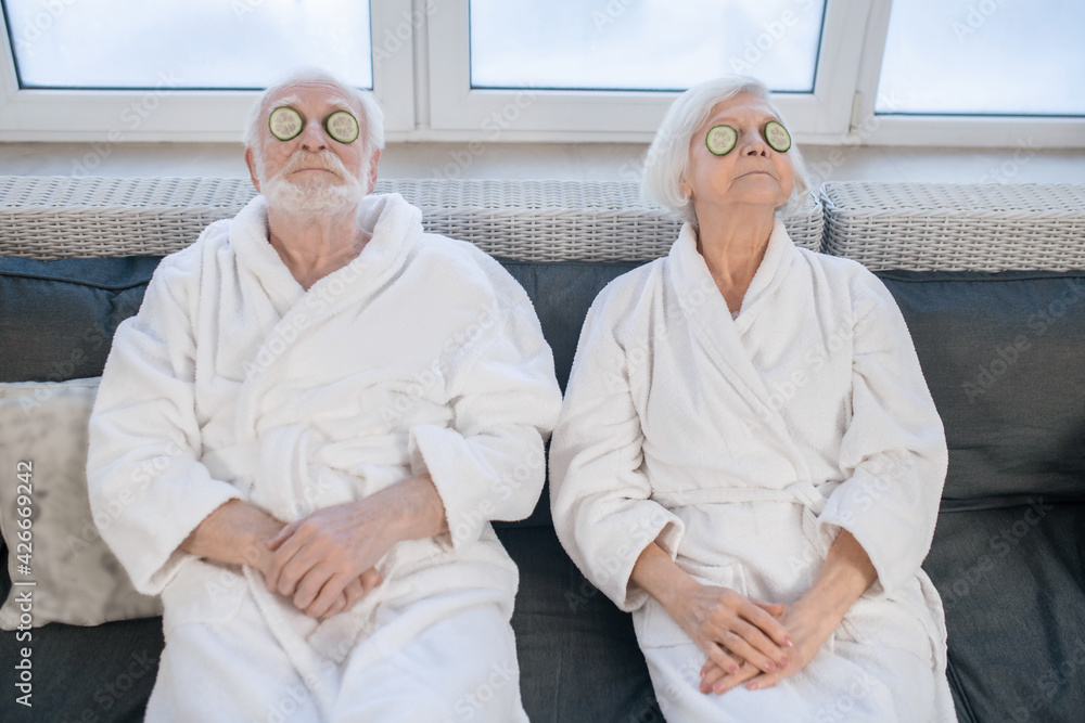 Senior couple in white robes enjoying spa procedures and having fun Senior couple in white robes enjoying spa procedures and having fun