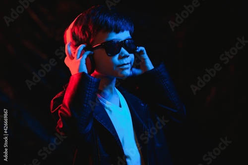 teen boy listening to music with headphones, neon light trending portrait. Looks at the camera