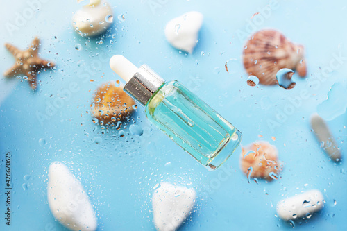 moisturizing face serum on a blue sea background with water drops and seashells.The concept of cosmetics with marine extracts