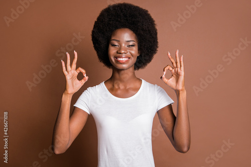 Portrait of friendly cheerful dark skin girl two hands fingers show okey symbol isolated on brown color background