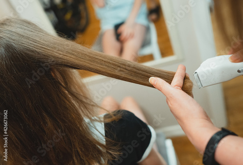 Mom cuts her daughter with a hair clipper at home.