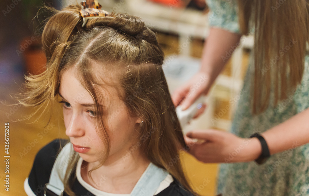 Fototapeta premium Mom cuts her daughter with a hair clipper at home.