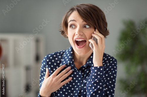 Portrait of attractive cheerful amazed shocked girl calling partner discussing great news at workplace workstation indoors