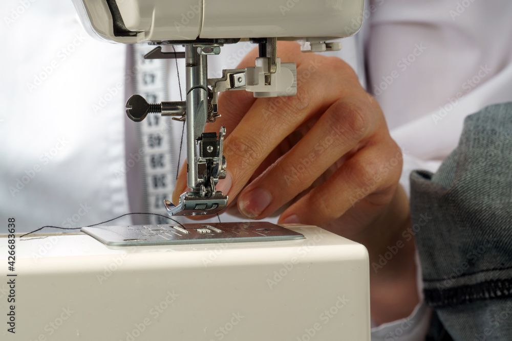 the process of threading the sewing machine needle. A tailor puts a thread in a needle
