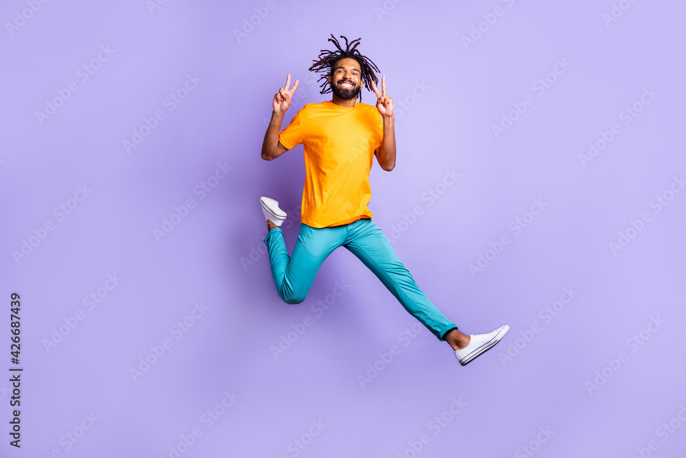 Full size photo of nice optimistic brunet guy jump show v-sign wear t-shirt pants isolated on lilac color background Full size photo of nice optimistic brunet guy jump show v-sign wear t-shirt pants isolated on lilac color background