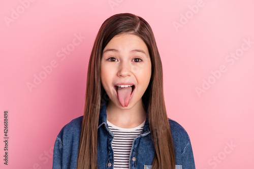 Photo portrait of wearing jeans jacket little girl grimacing showing tongue isolated on pastel pink color background