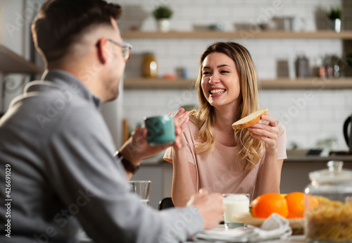 Beautiful woman enjoying in breakfast with her boyfriend. Happy young couple drinking coffee and eating sandwich at home