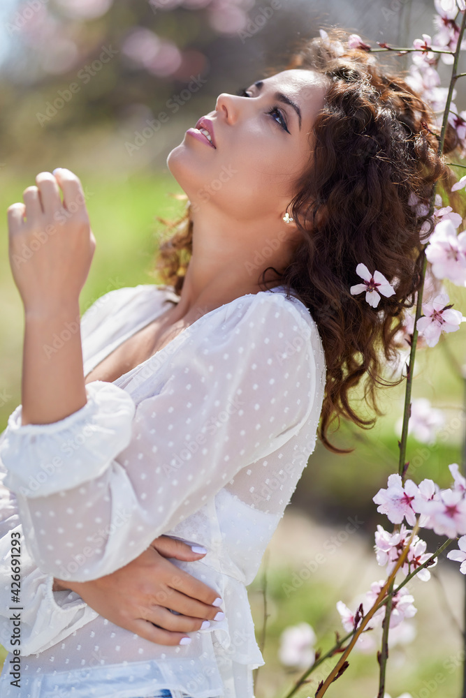 spring portrait of a beautiful woman with curly hair next to tree flowers spring portrait of a beautiful woman with curly hair next to tree flowers