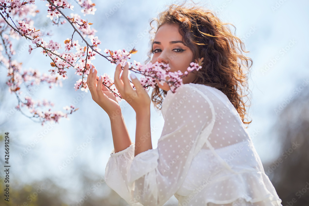 spring portrait of a beautiful woman with curly hair next to tree flowers
