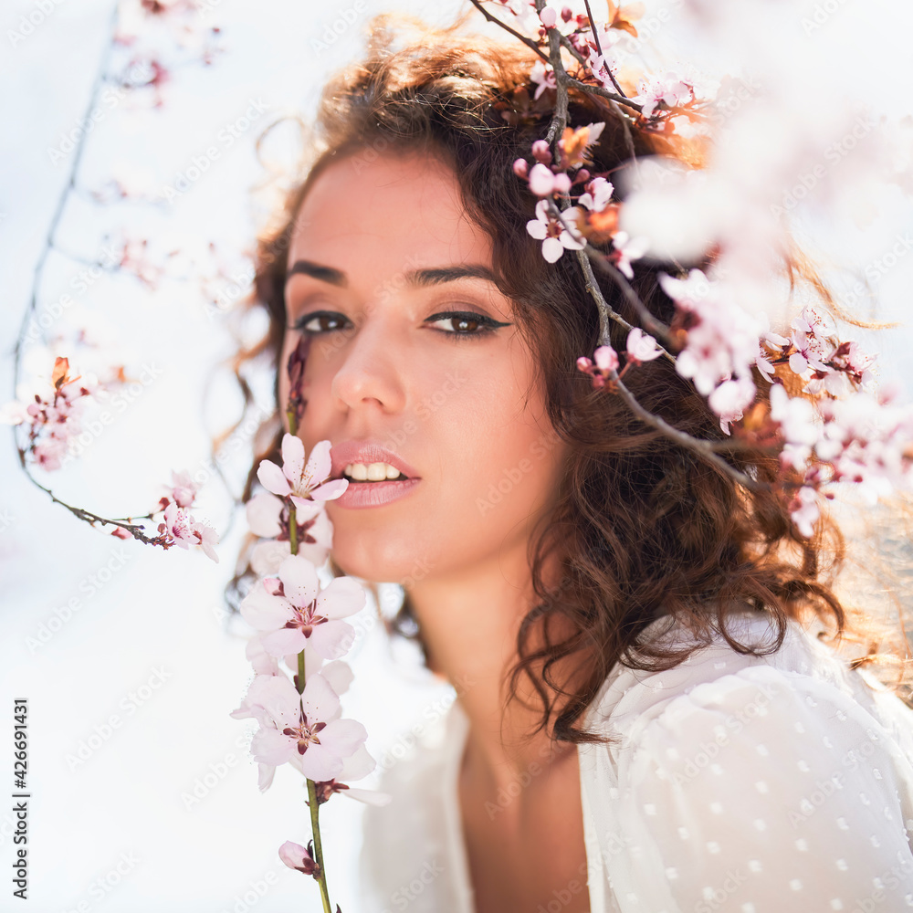 spring portrait of a beautiful woman with curly hair next to tree flowers