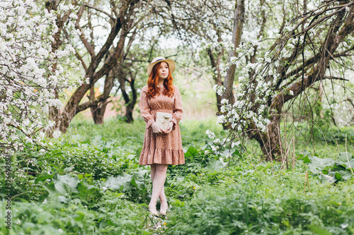 Red-haired girl walks in a spring blooming apple orchard