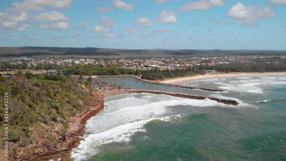 Aerial view away from waves hitting the shore of the Evans Head village, sunny, summer day, in Australia - reverse, drone shot Aerial view away from waves hitting the shore of the Evans Head village, sunny, summer day, in Australia - reverse, drone shot