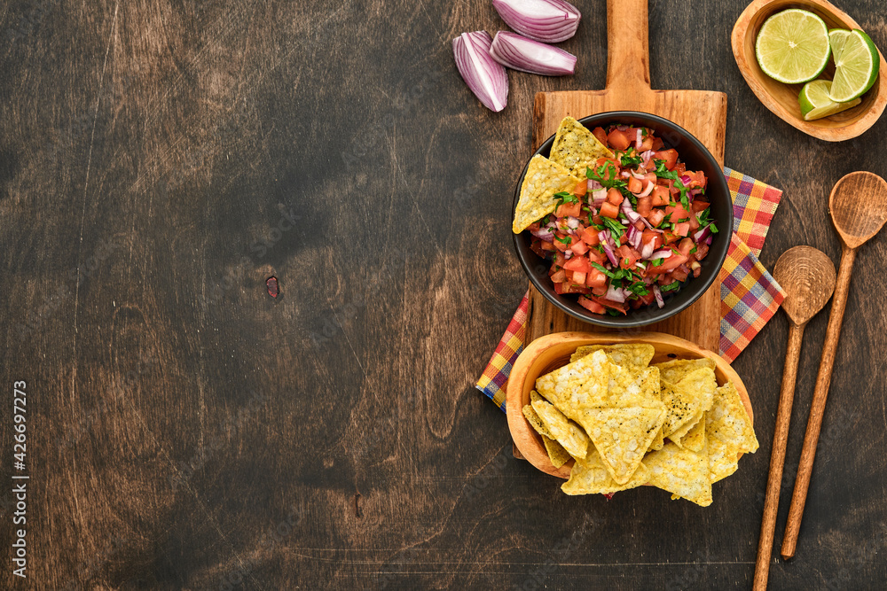 Traditional Mexican tomato sauce salsa with nachos and ingredients tomatoes, chile, garlic, onion on dark old wooden background. Concept of Latin American and Mexican food. Mock up.