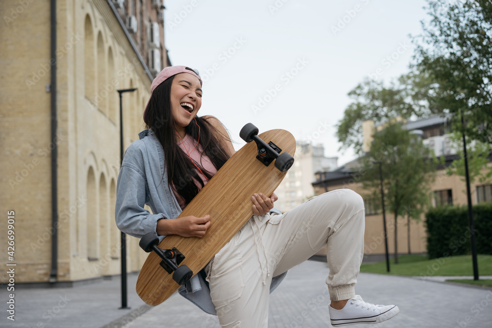 Happy emotional asian woman holding skateboard, dancing, having fun outdoors. Inspiration, positive lifestyle concept