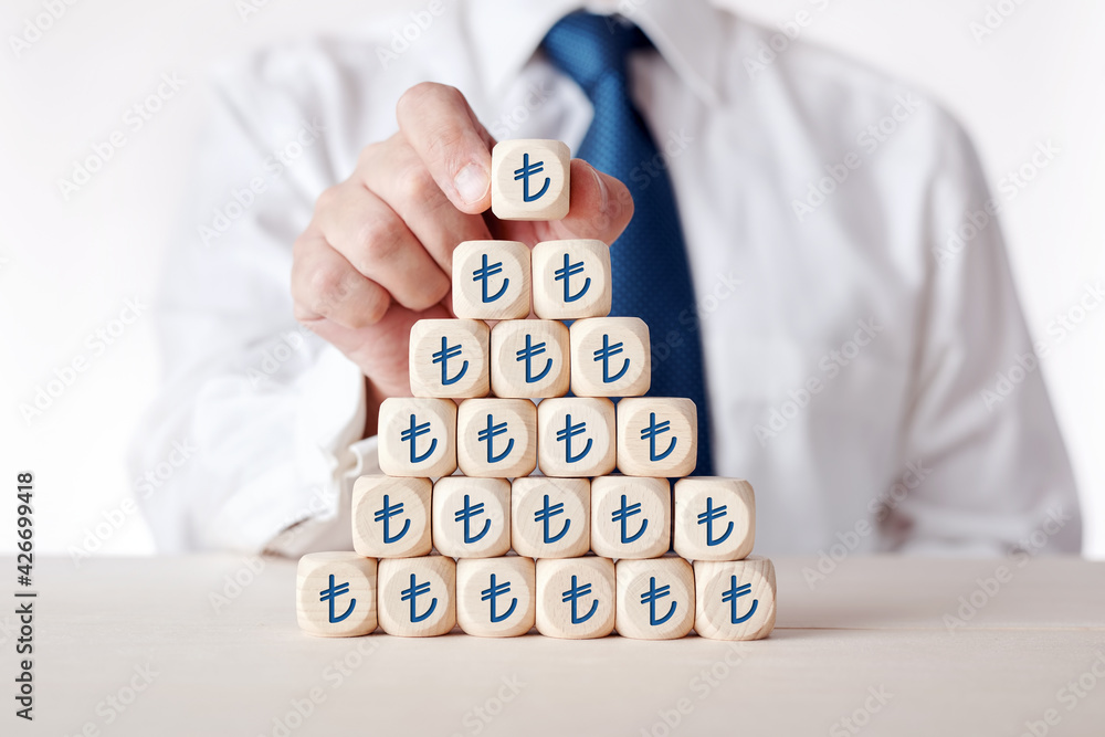 Businessman placing cube with Turkish Lira symbol on top of tiered wooden cubes. Businessman placing cube with Turkish Lira symbol on top of tiered wooden cubes.