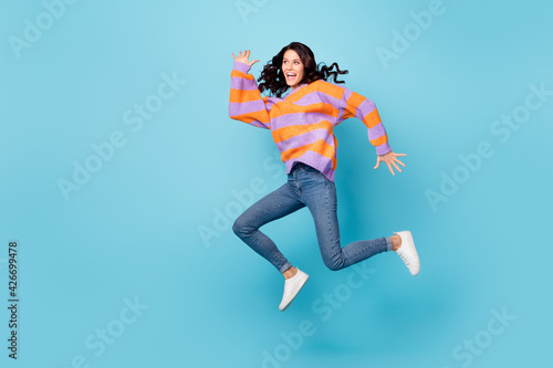 Full length body size view of pretty overjoyed cheerful wavy-haired girl jumping running having fun isolated over bright blue color background