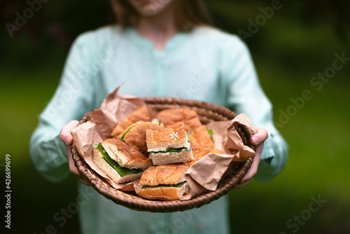 Young girl holds basket with homemade vegetarian sandwiches in the garden. Healthy snack with flatbread, cheese dip and fresh wild garlic leaves. Selective focus. Copy space.