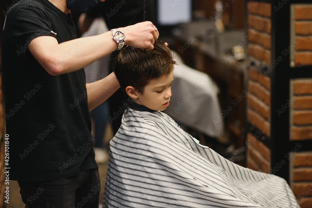 A little cute boy sits in a hairdresser's at the stylist's, a schoolchild is getting hair cut in a beauty salon, a child at a barbershop's, a short men's haircut. A little cute boy sits in a hairdresser's at the stylist's, a schoolchild is getting hair cut in a beauty salon, a child at a barbershop's, a short men's haircut.