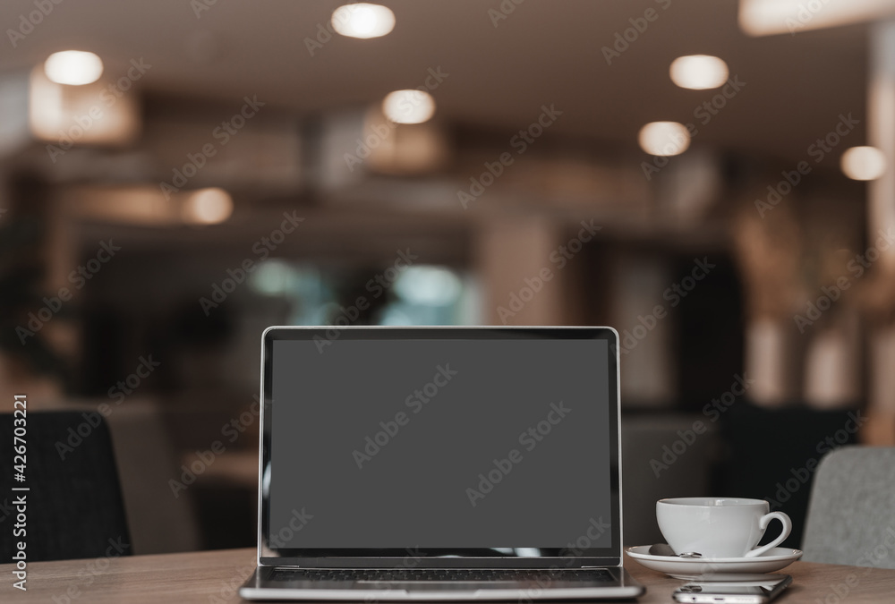 Mockup of laptop computer with empty screen with coffee cup and smartphone on table of the coffee shop background Mockup of laptop computer with empty screen with coffee cup and smartphone on table of the coffee shop background