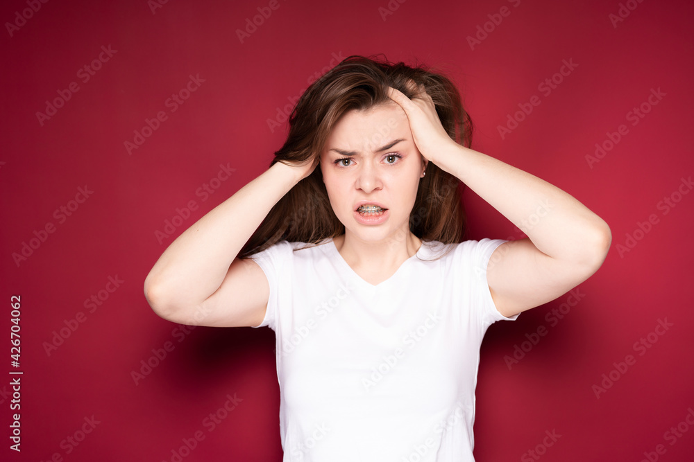 Pretty girl gets annoyed with headache after getting braces. Isolated on red background Pretty girl gets annoyed with headache after getting braces. Isolated on red background