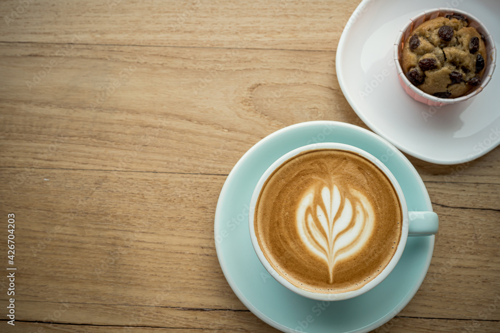Obraz premium Hot coffee latte with latte art milk foam in cup mug and Homemade Banana cup cake on wood desk on top view. As breakfast In a coffee shop at the cafe,during business work concept