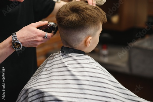 Side view of cute little boy getting haircut by hairdresser at the barbershop