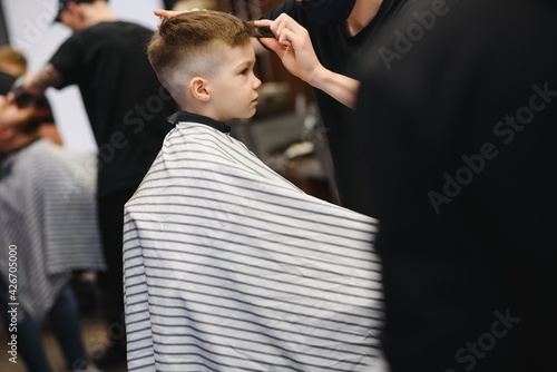 Side view of cute little boy getting haircut by hairdresser at the barbershop