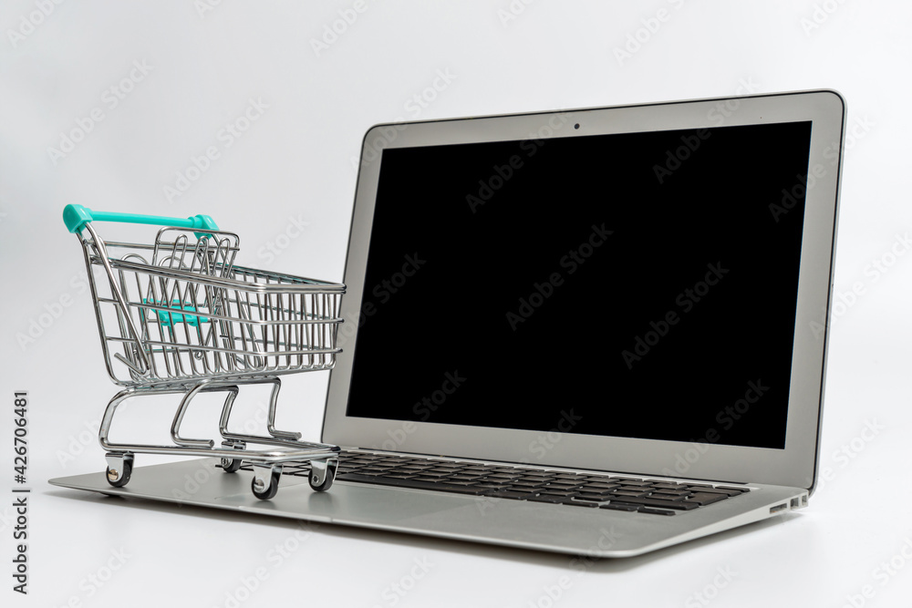 miniature shopping cart on laptop, isolated on light background miniature shopping cart on laptop, isolated on light background