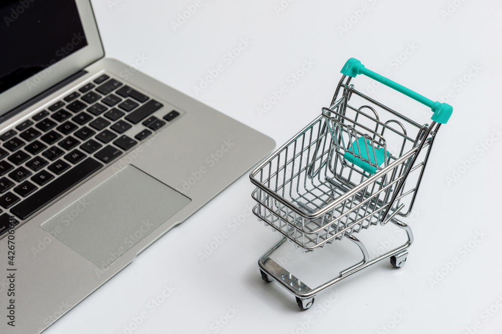 shopping cart next to laptop, isolated on light background