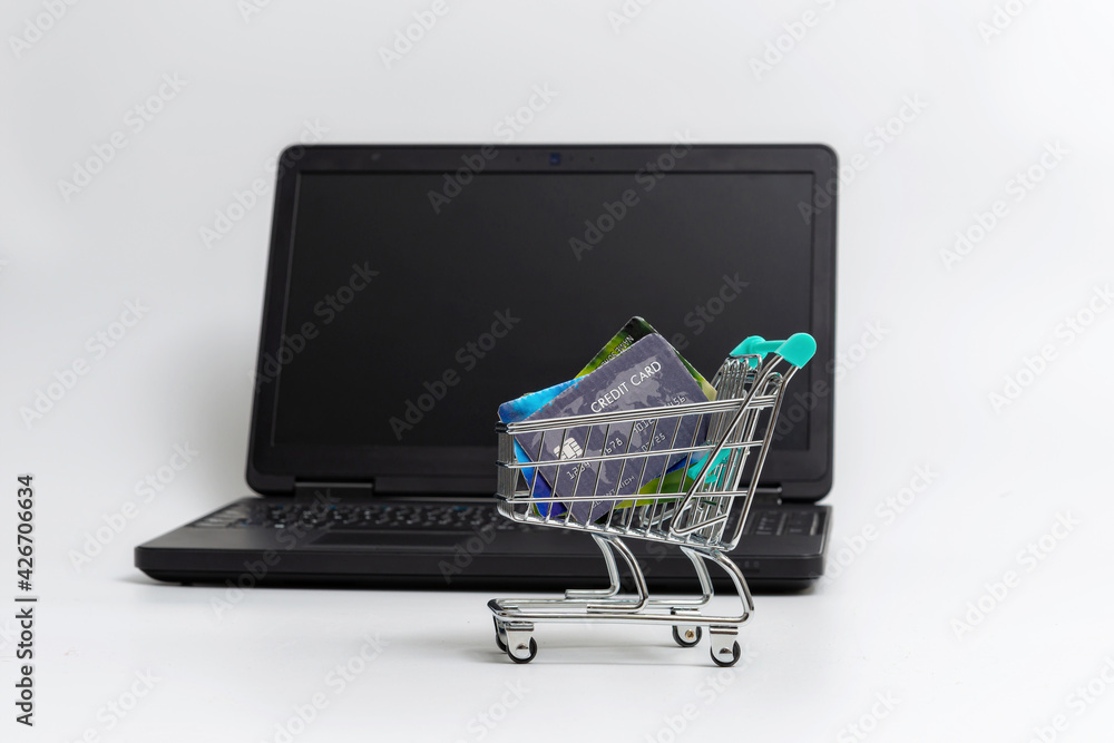 miniature shopping cart with credit cards next to laptop, isolated on light background