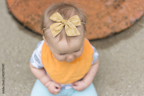 10 month old baby with yellow bow in hair sitting on front stoop of home; fine baby hair