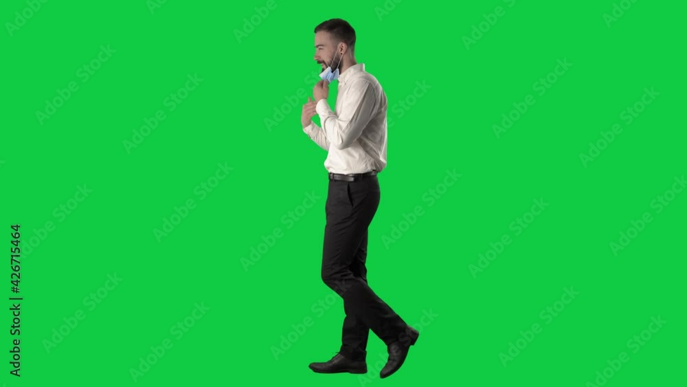 Side view of walking businessman removing face mask revealing face and greeting. Full body on green screen chroma key background. Side view of walking businessman removing face mask revealing face and greeting. Full body on green screen chroma key background.