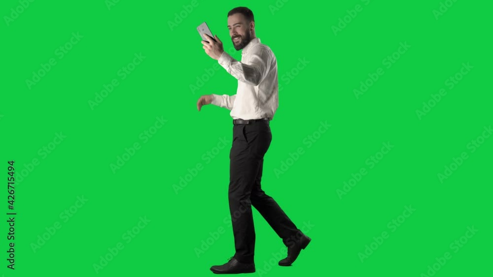 Side view of happy walking business man filming selfie videos greeting and winking. Full body on green screen chroma key background. Side view of happy walking business man filming selfie videos greeting and winking. Full body on green screen chroma key background.