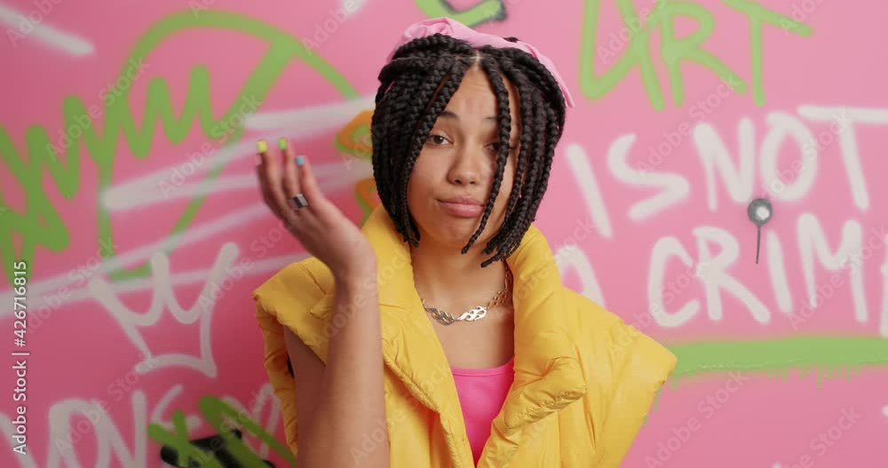 Puzzled frustrated ethnic woman makes face palm has tired displeased expression dressed in yellow vest poses against colorful graffiti wall bein fed up of everything. Teenagers lifestyle concept