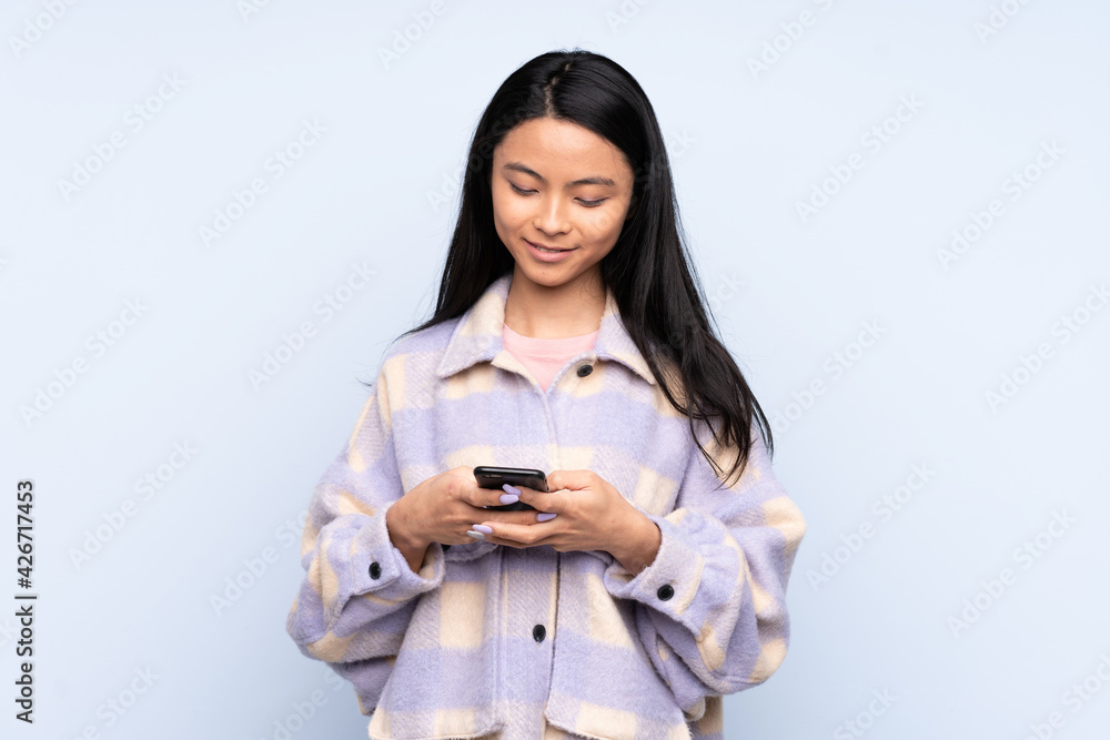 Teenager Chinese woman isolated on blue background sending a message with the mobile Teenager Chinese woman isolated on blue background sending a message with the mobile