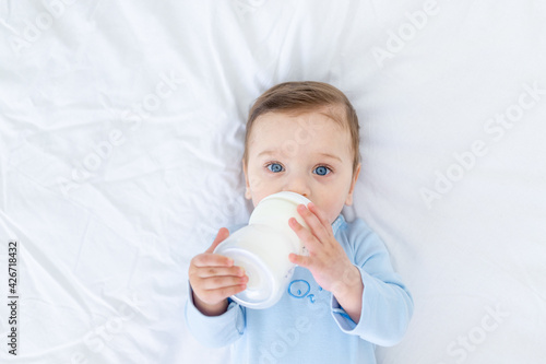 baby boy eats milk from a bottle on the bed before going to bed in a blue bodysuit, baby food concept