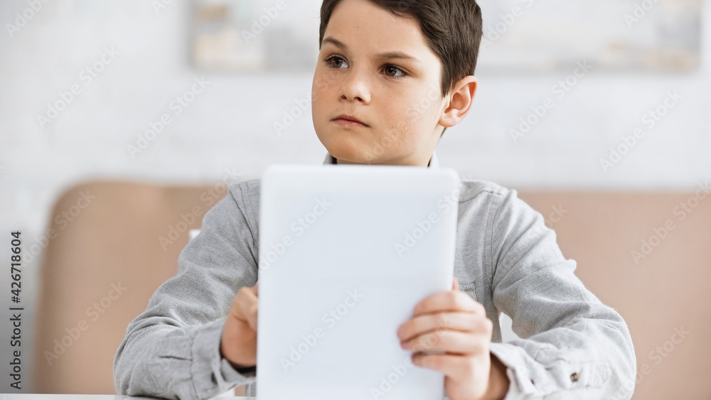 Preteen boy holding digital tablet on blurred foreground during online education. Preteen boy holding digital tablet on blurred foreground during online education.