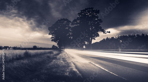 Düstere Lichtstreifen in Langzeitbelichtung an einer Landstraße. Eine mysteriöse, düstere Straße mitten im Wald im schönen Lubkowo in Polen. Düsterer Feldweg, Feldstraße photo