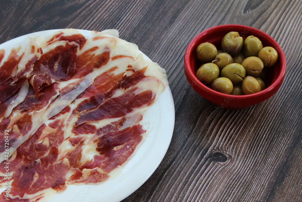 Iberian ham with bowl of olives on wooden background